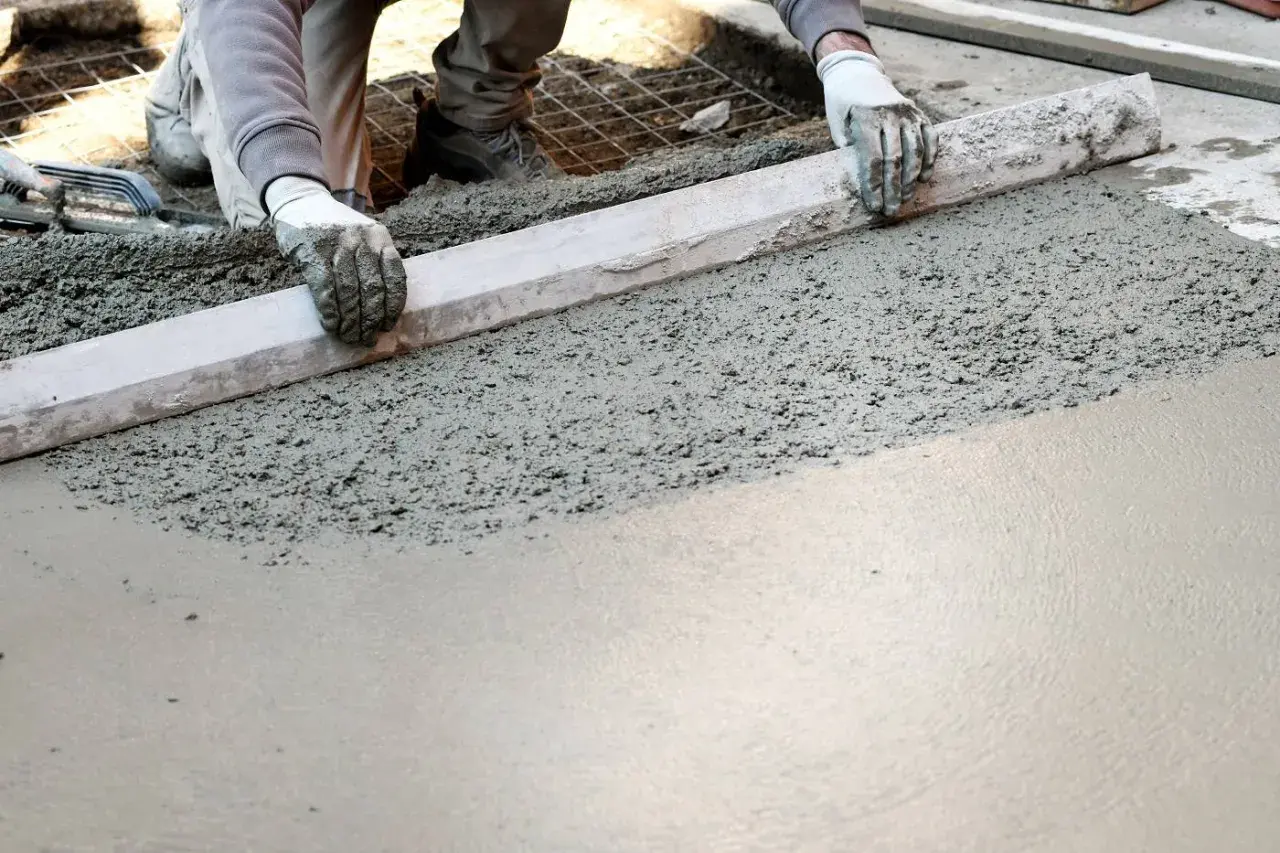 Ręce w rękawiczkach wyrównują świeży beton. Powstaje gładka powierzchnia, która wkrótce stanie się solidnym kubikiem betonu.