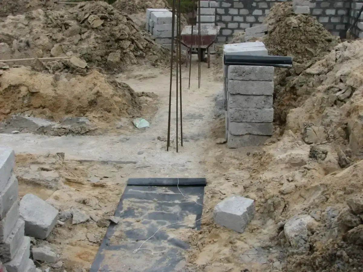 Budowa domu w toku. Widoczne wykopy, zbrojenie i materiały budowlane, tworzące fundamenty domu.