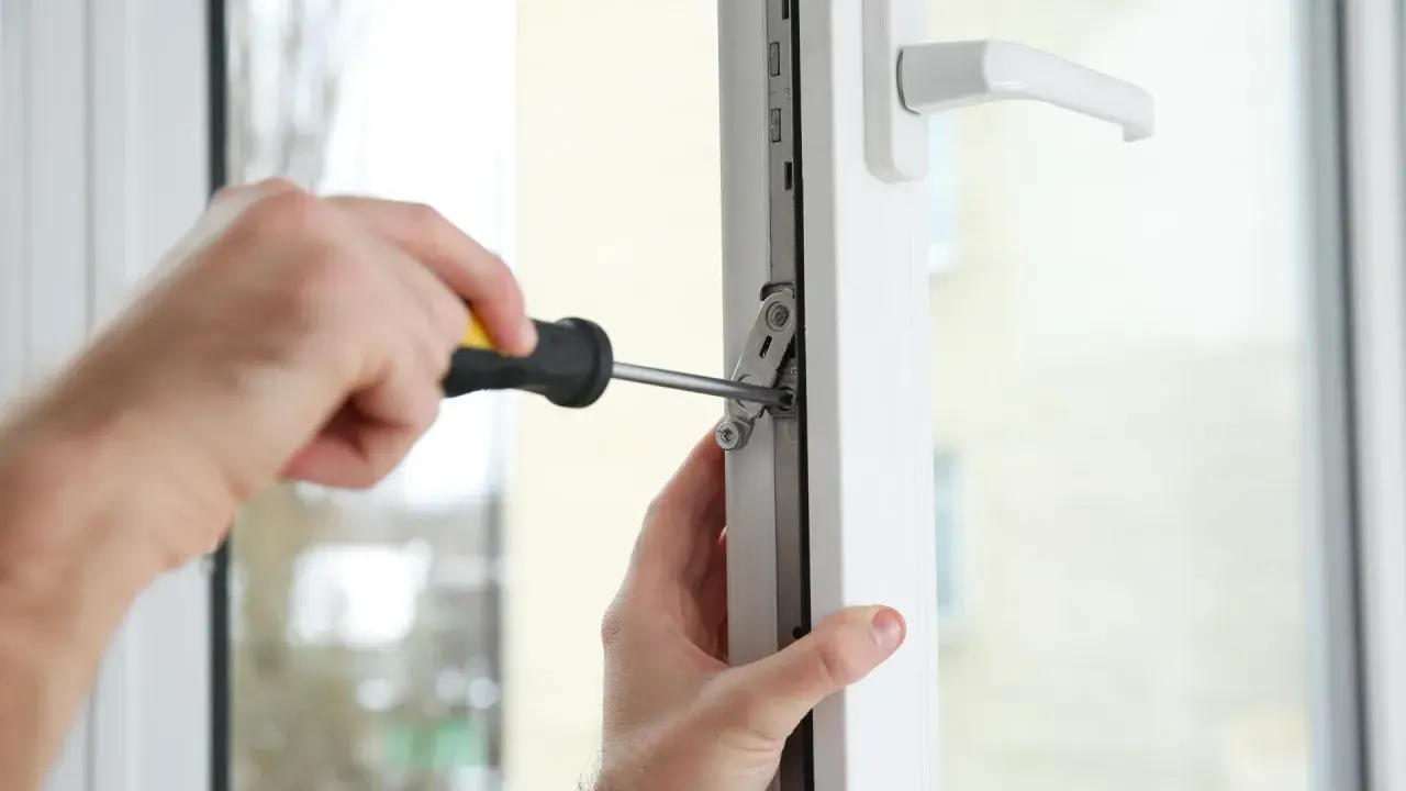 Regulacja docisku okna. Ręce majsterkowicza dokręcają śrubę w mechanizmie okna, aby zapewnić jego szczelność.