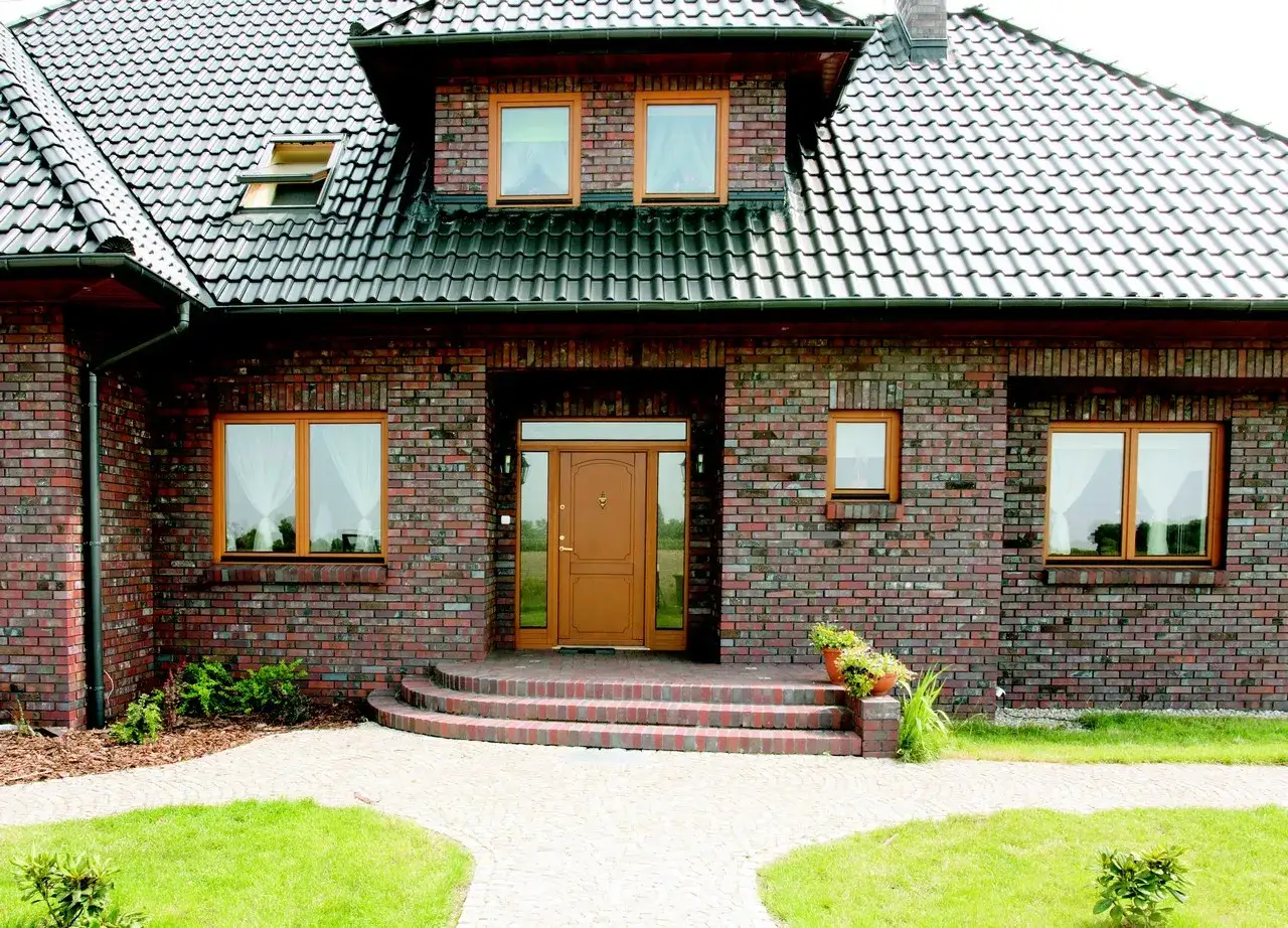 Nowy dom z cegły, z brązowymi oknami i drzwiami, z tarasem i ścieżką.
