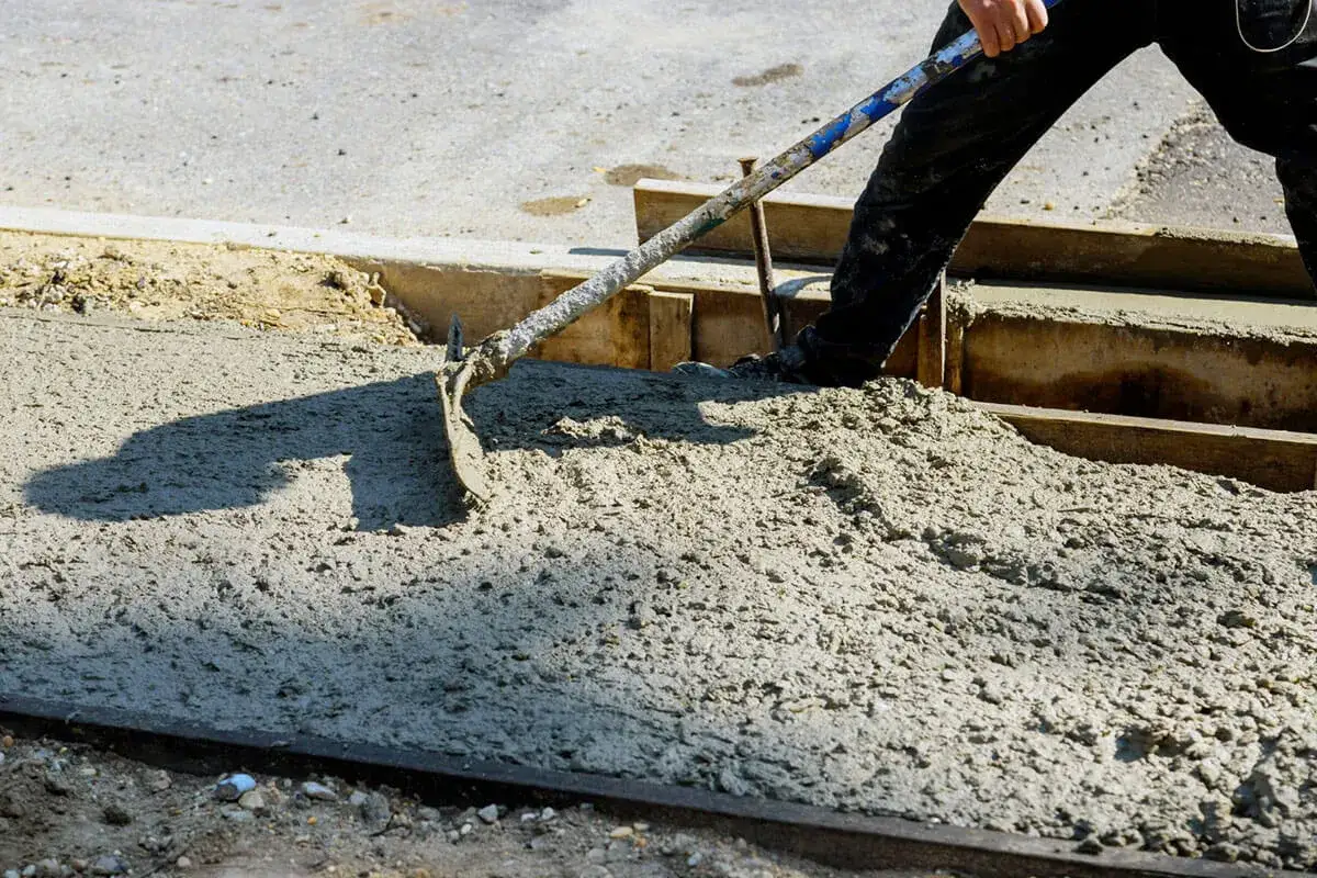 Robotnik rozprowadza świeży beton łopatą. To właśnie beton, mieszanka cementu, kruszywa i wody, tworzy trwałe konstrukcje.