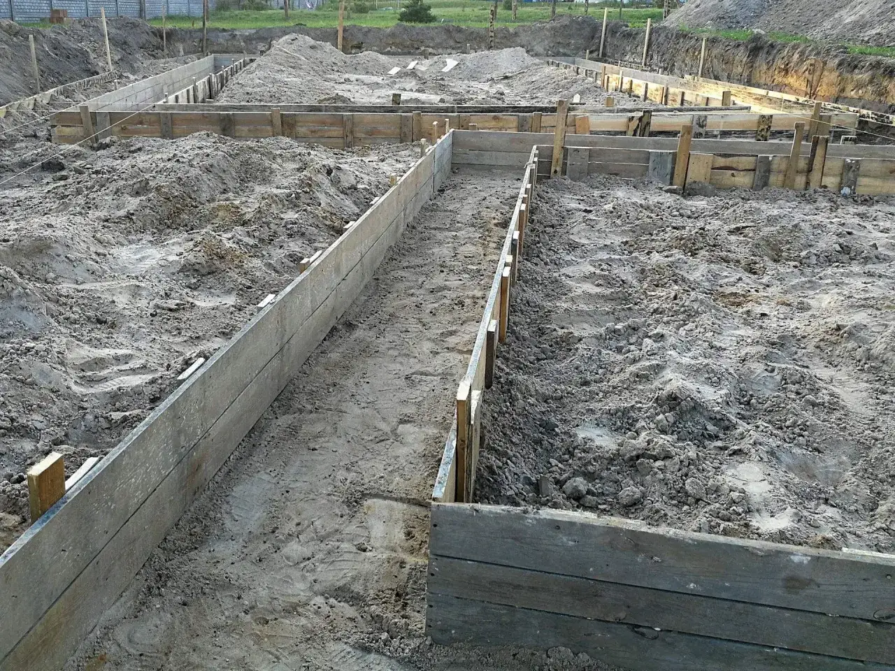 Drewniane szalunki wyznaczają przyszłe ściany fundamentów. Czekają na odpowiedni beton na fundament, który zapewni stabilność budowli.