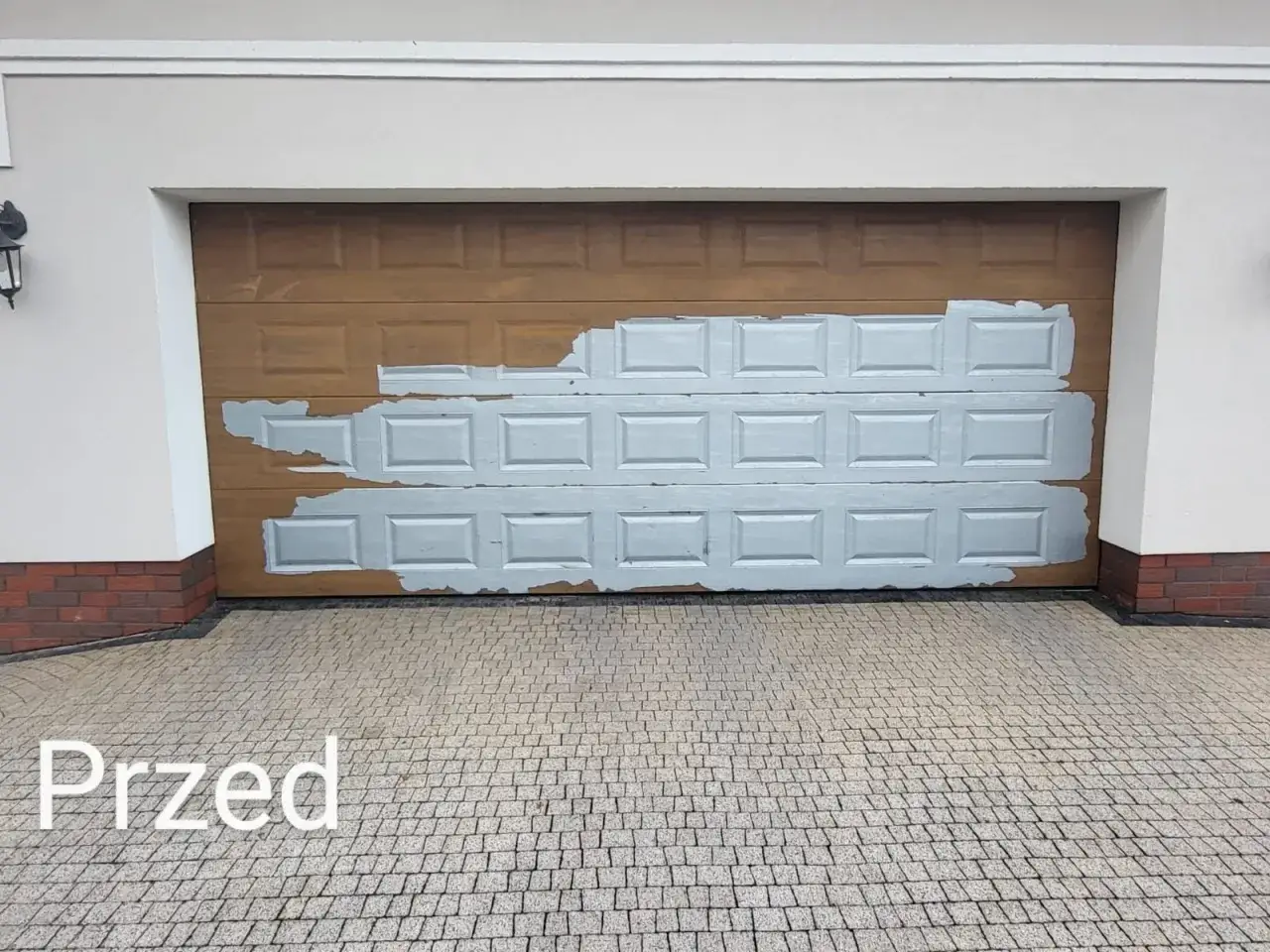 Przed wymianą okleiny na bramie garażowej. Widoczna stara, brązowa okleina z fragmentami szarej farby.