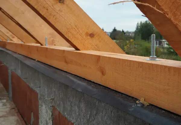Zbrojenie wieńca pod murłatę: drewniane krokwie mocowane śrubami do betonowego wieńca, przygotowanie do budowy dachu.