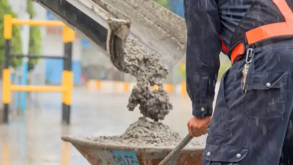 Robotnik w deszczu wylewa świeży beton do taczki. To właśnie jest beton – mieszanka cementu, kruszywa i wody.