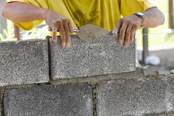 Murarz układa bloczki betonowe fundamentowe, tworząc solidną podstawę.