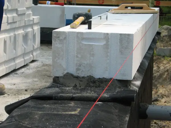 Budowa domu: układanie bloczków z betonu komórkowego, montaż izolacji poziomej fundamentów, poziomica i kielnia.