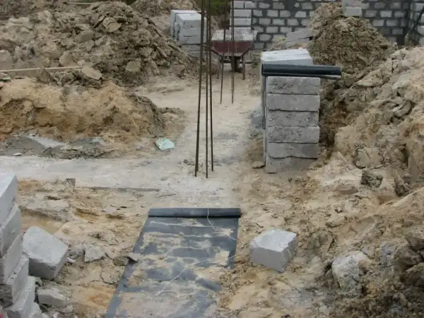 Budowa domu w toku. Widoczne wykopy, zbrojenie i materiały budowlane, tworzące fundamenty domu.